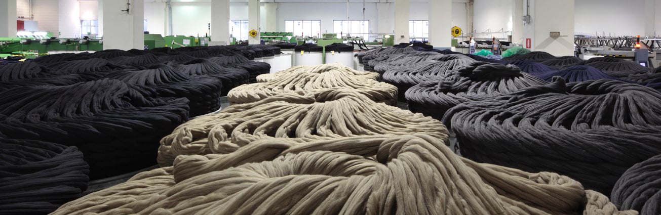 Grandi cumuli di nastri di lana beige e grigio scuro sul pavimento di un luminoso stabilimento tessile