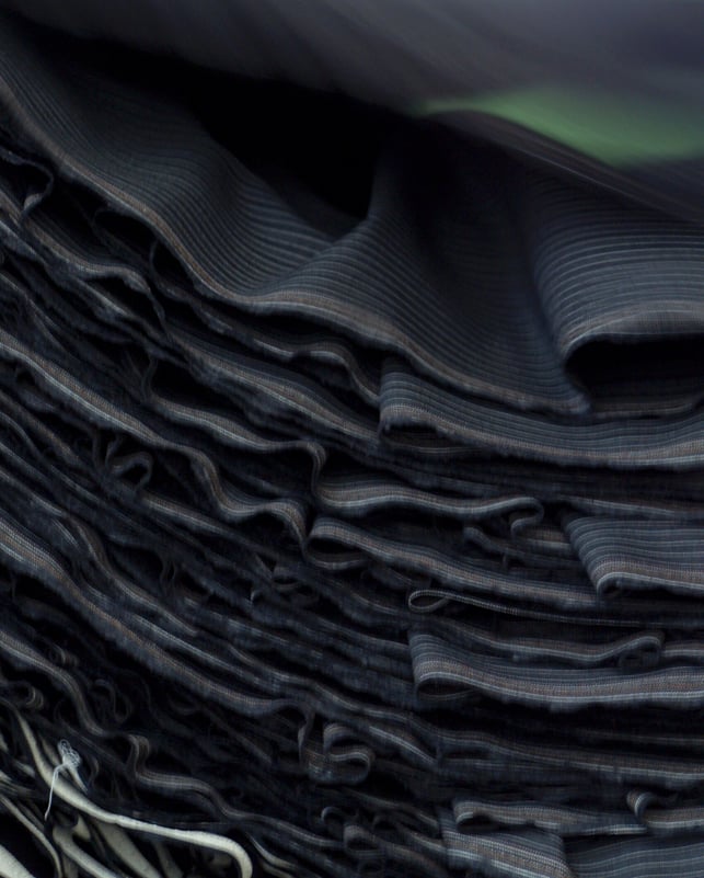 Close-up of a stack of folded dark pinstriped fabric with wavy edges and thin light stripes