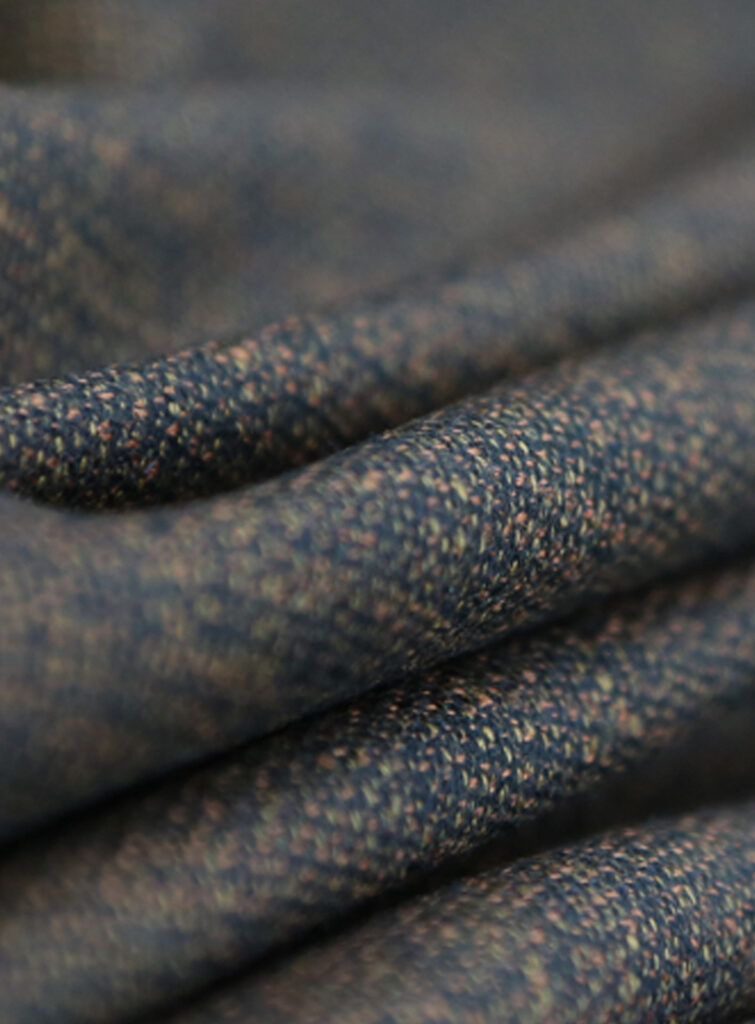 Close-up of draped blue woven wool fabric with orange and beige flecks, soft folds in shallow focus
