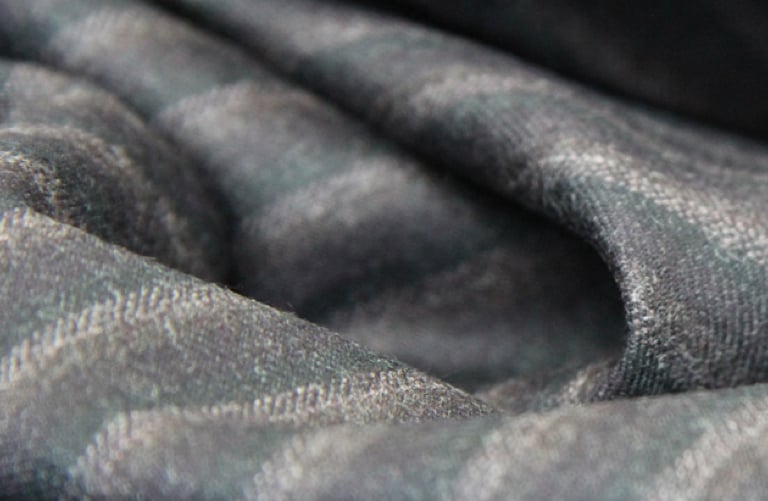 Close-up of soft folds in a gray woolen fabric with a subtle diagonal weave and stripe pattern
