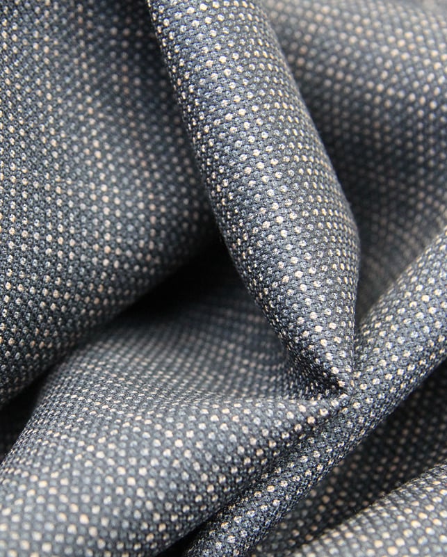 Close-up of draped blue-gray woolen fabric with a fine woven micro-dot pattern in beige