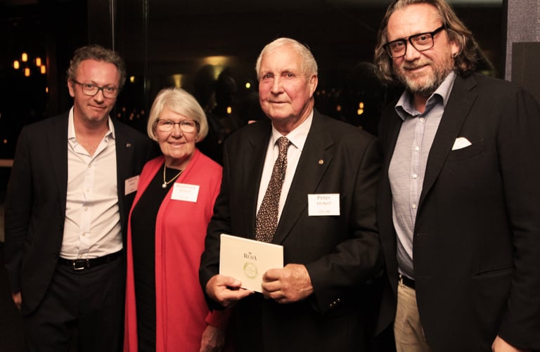 Four people in formal attire pose together at an event; the man holding a small booklet wears a Peter name tag