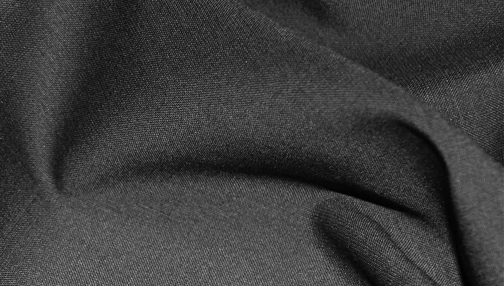 Close-up of dark charcoal grey woven fabric with soft folds and visible fine texture