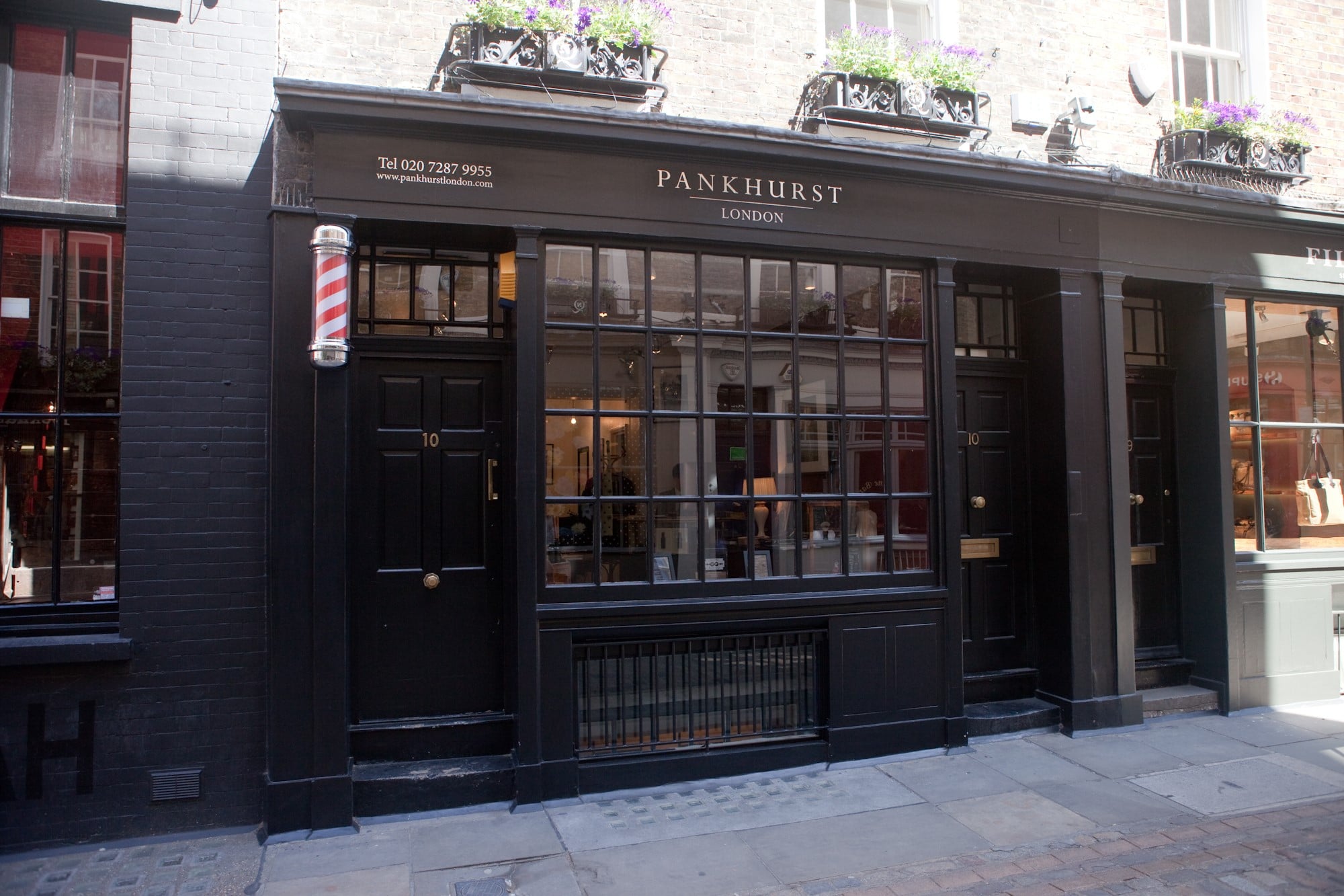 Black storefront of Pankhurst London with a barber pole, large paned window and flower boxes above