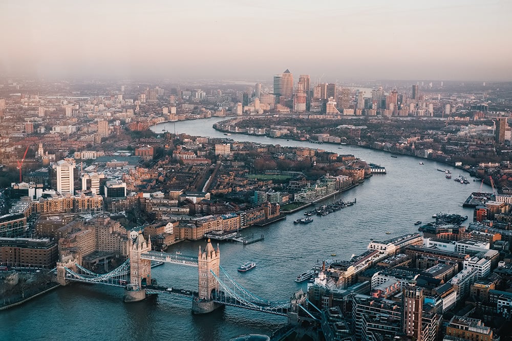 Aerial view of Tower Bridge and the River Thames winding through London at dusk, with skyscrapers beyond
