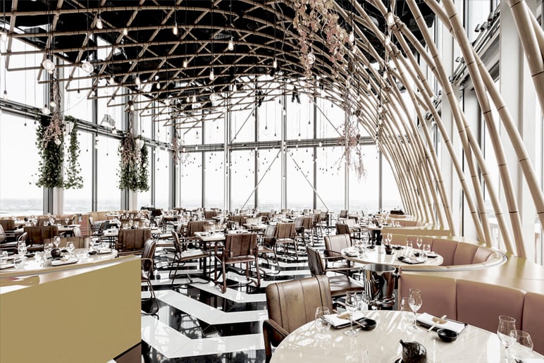 Restaurant interior with curved bamboo-like beams, floor-to-ceiling windows and tables on a black and white floor