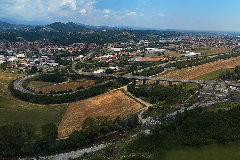 Veduta aerea di un viadotto su un fiume, con una cittadina, campi e colline boscose sullo sfondo