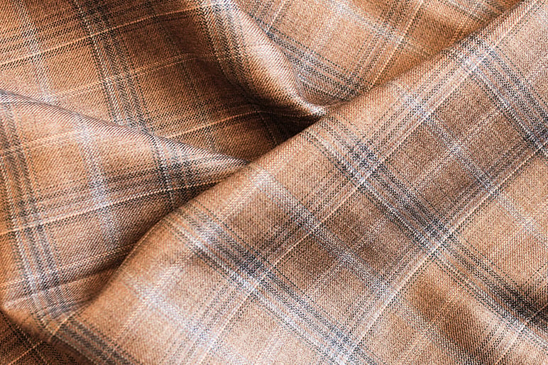 Primo piano di tessuto in lana marrone drappeggiato con motivo a quadri beige, blu e bianco