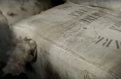 Close-up of a worn burlap wool bale stamped with a sheep-shaped map outline and partly legible lettering