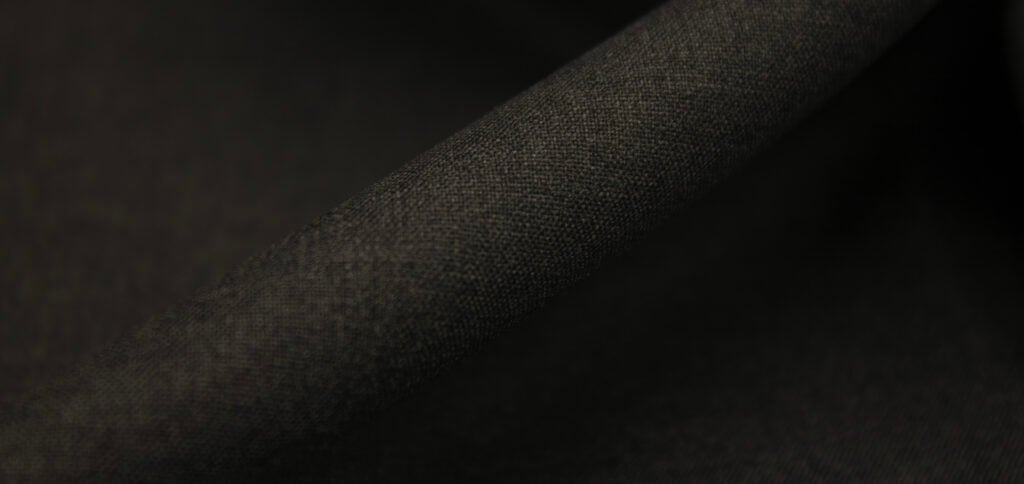 Close-up of dark charcoal woolen fabric with a fine woven texture, folded diagonally in soft light
