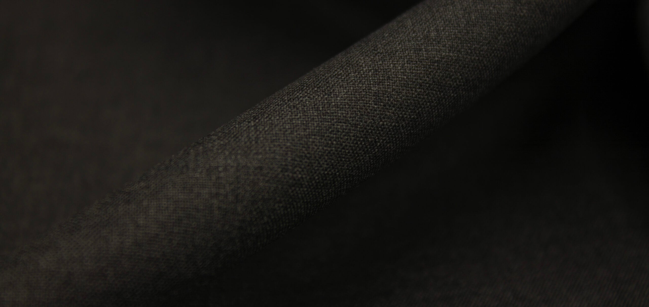 Close-up of dark charcoal woolen fabric with a fine woven texture, folded diagonally in soft light