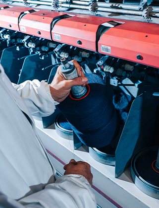 Worker in a white coat handles a spool of dark blue yarn on a red textile machine