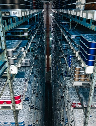 Tall warehouse aisle with metal shelving holding stacked trays of fabric rolls in grey, blue and red