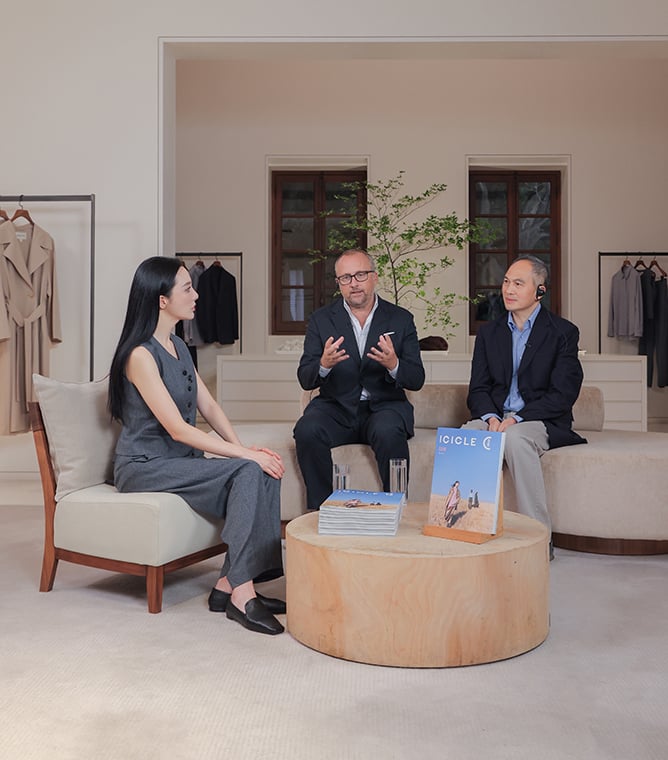 Three people talk in a boutique, seated around a wooden table with ICICLE magazines on it