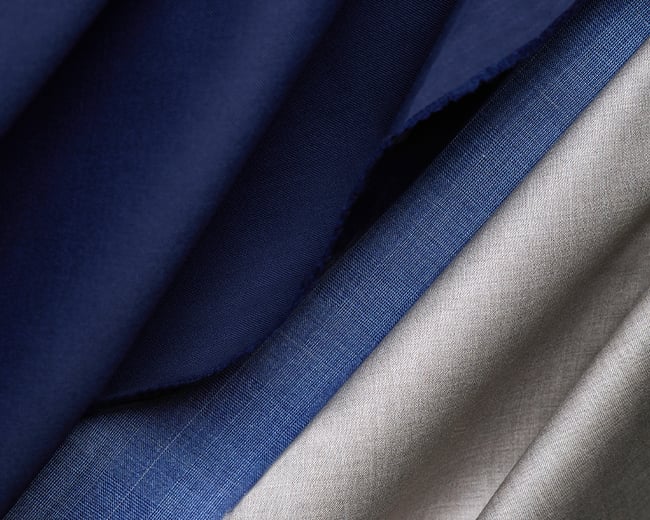Close-up of folded navy blue, bright blue and light grey wool fabrics with visible weave texture
