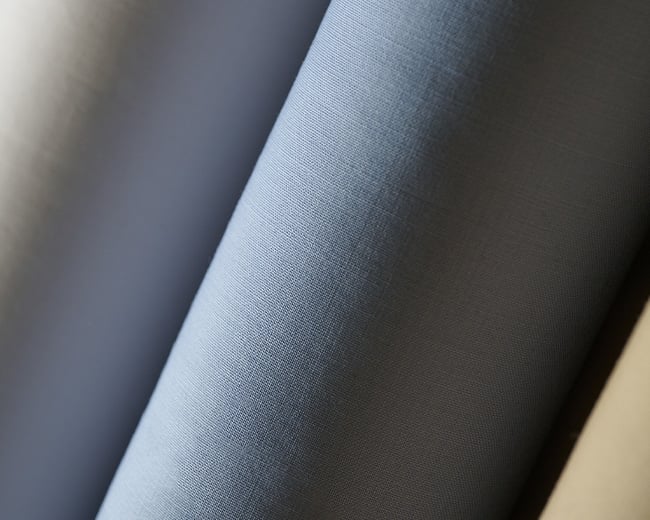 Close-up of a light blue woven fabric draped in soft folds, with visible weave texture in soft light