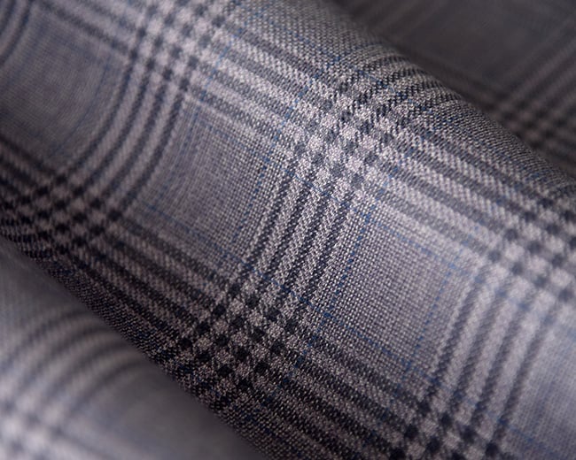 Close-up of gray wool fabric with a dark Glen plaid pattern and thin blue lines, loosely rolled