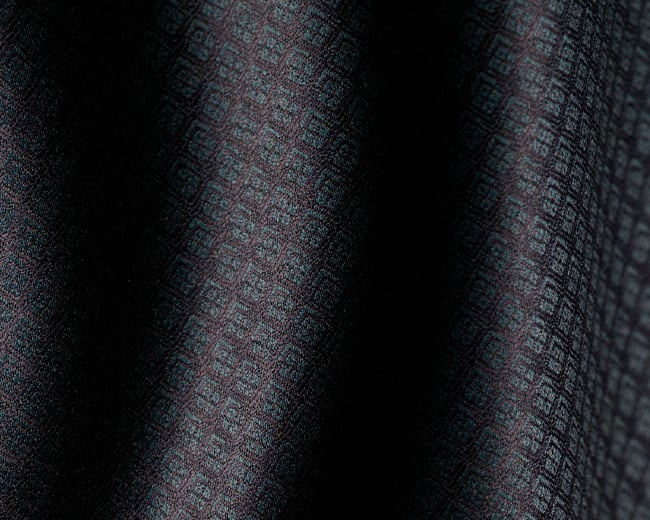 Close-up of dark draped fabric with a small geometric woven pattern in blue-grey and burgundy tones