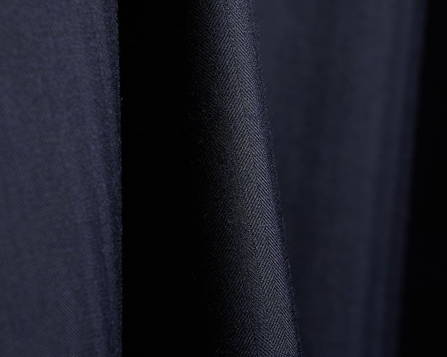 Close-up of navy blue wool fabric with a fine herringbone weave, falling in soft folds
