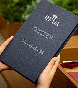 Hands holding a dark blue REDA book titled "Icons of Style – Milano Boost me up"