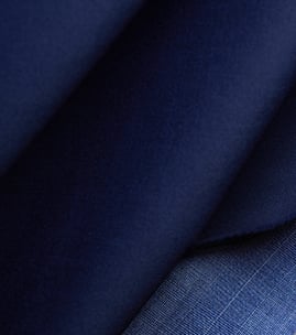 Close-up of navy blue woolen fabric folded softly, with a lighter blue fine-checked weave visible at the corner