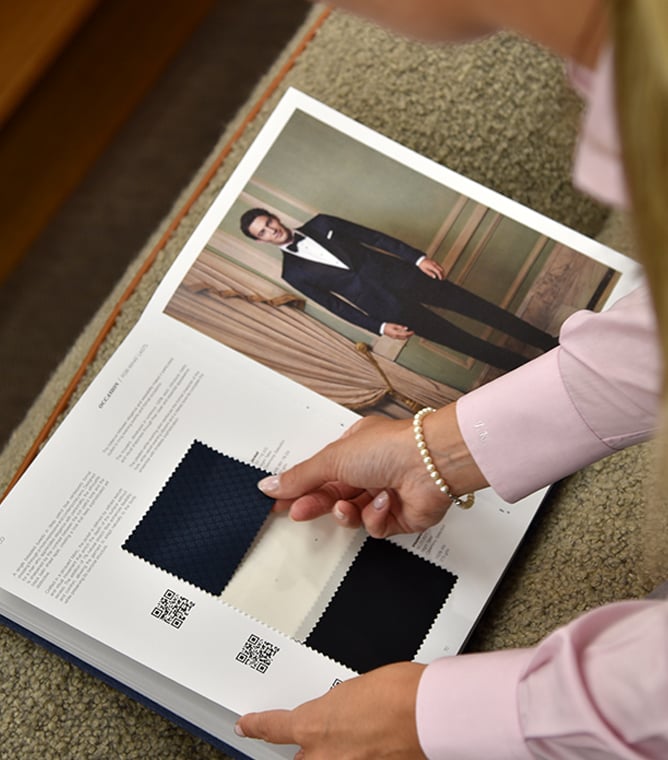 Woman in pink shirt touches fabric swatches in a swatch book showing a man in a navy tuxedo