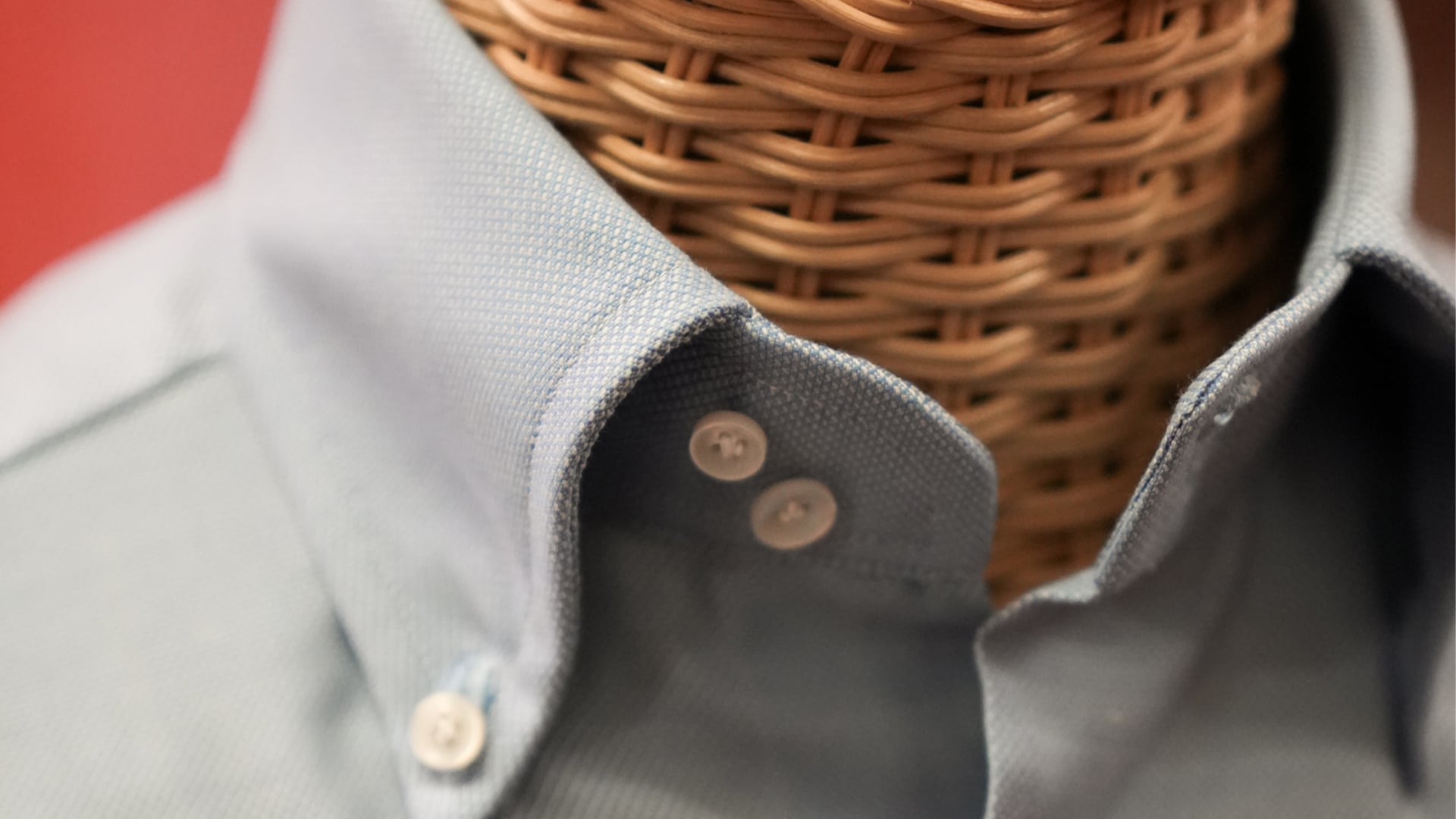 Primo piano di un colletto button-down azzurro in tessuto texturizzato su un manichino in vimini
