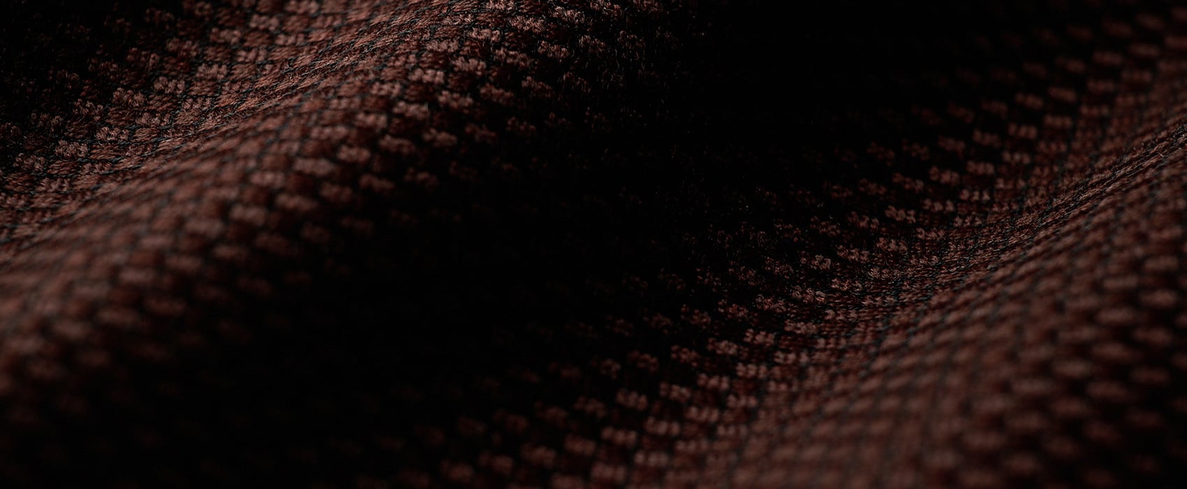 Close-up of dark brown woven wool fabric with a fine textured pattern, softly folded in shadow