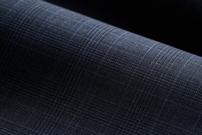 Close-up of dark navy wool fabric with a subtle light blue glen check pattern, draped in soft folds
