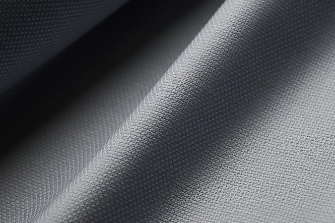 Close-up of gray woven fabric with a fine texture, draped in soft folds with light and shadow