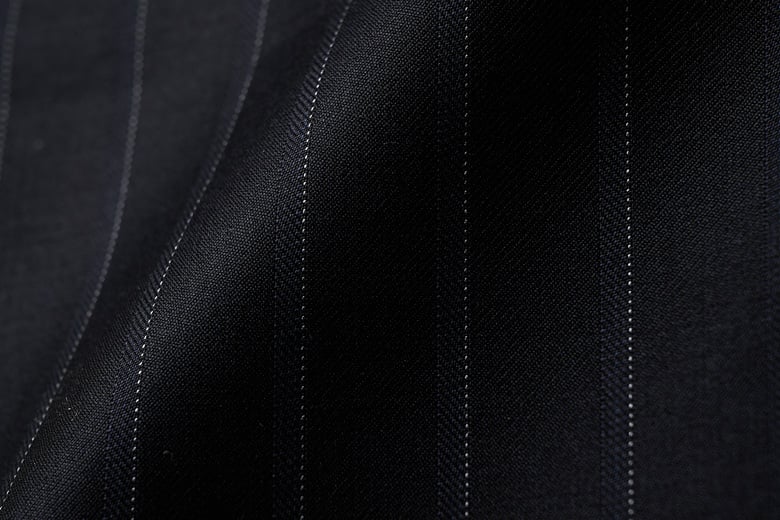 Close-up of dark navy wool fabric with thin white pinstripes, softly draped in folds