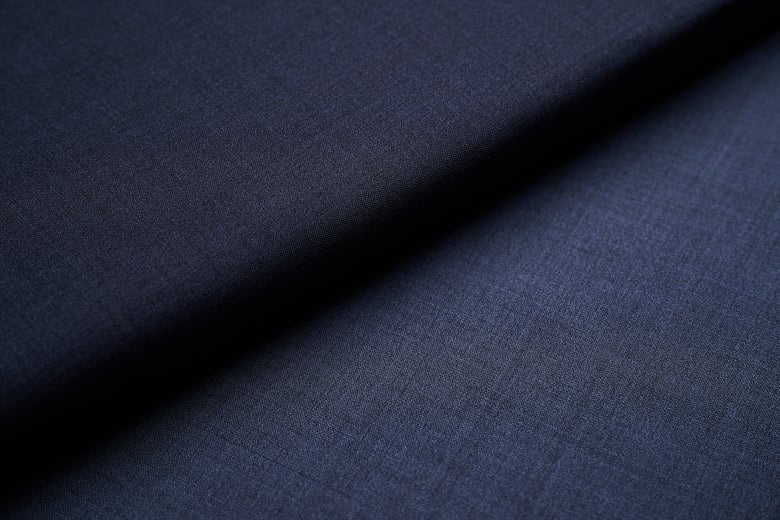 Close-up of navy blue wool fabric with a fine weave, draped in a soft diagonal fold with shadow