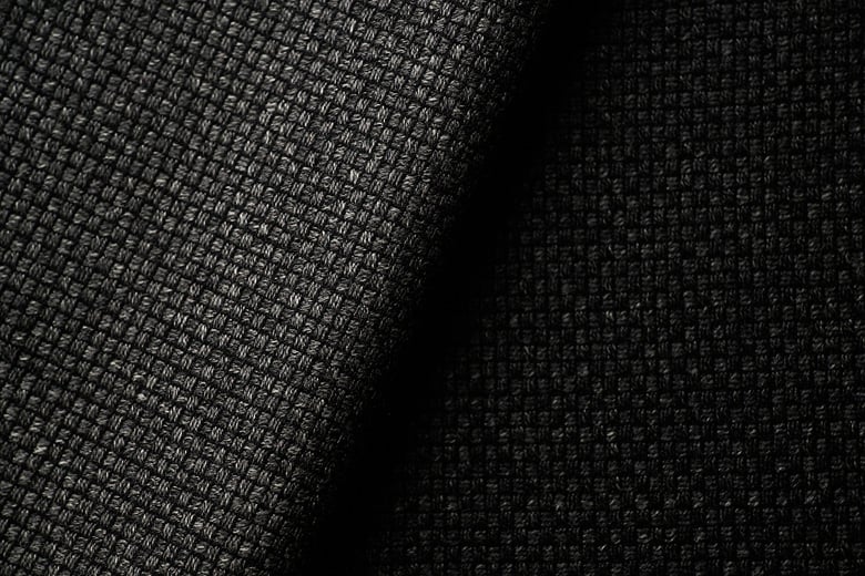 Close-up of dark charcoal woven wool fabric with a visible basketweave texture, folded in soft light