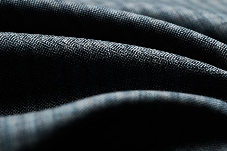 Close-up of dark blue-grey woolen fabric with a fine woven texture, draped in soft folds