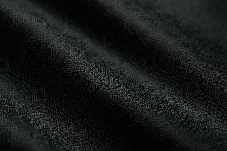 Close-up of black wool fabric with a subtle woven geometric diamond pattern and soft folds