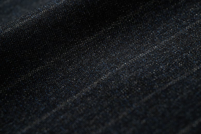 Close-up of dark navy wool fabric with a fine woven texture and subtle lighter stripes