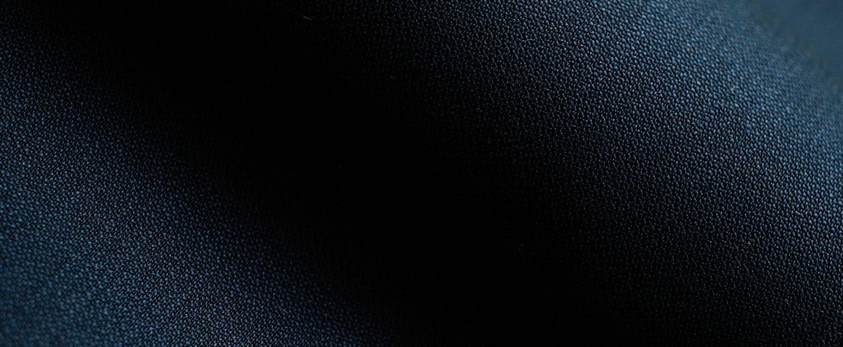 Close-up of dark navy wool fabric with a fine woven texture, draped in soft folds with light and shadow