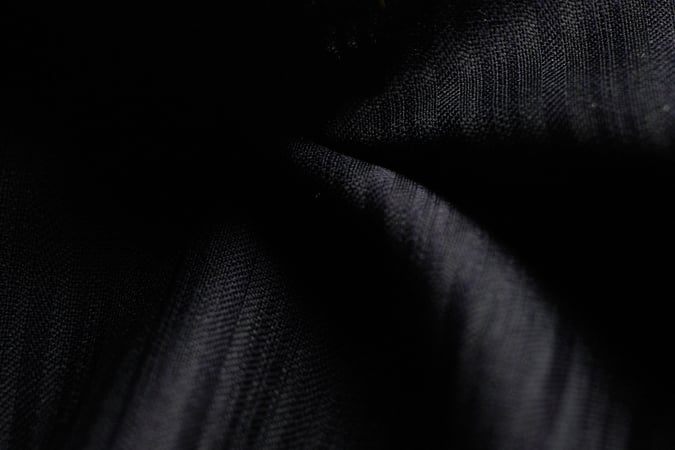 Close-up of dark black fabric with soft folds and a fine woven texture, lit by subtle highlights