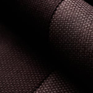 Close-up of dark brown woven fabric with a fine basketweave texture, softly lit with folds in shadow