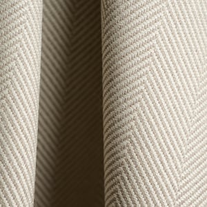 Close-up of cream herringbone woven fabric draped in soft folds, showing its textured zigzag pattern