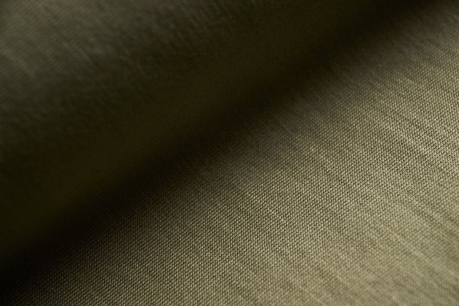 Close-up of olive green jersey fabric with a fine knit texture, with soft light and shadow across the surface