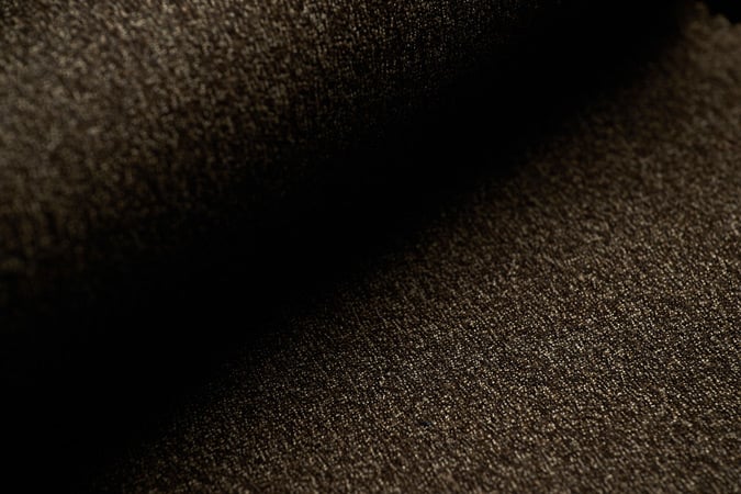 Close-up of dark brown flannel wool fabric with a fine speckled texture, softly lit with deep shadows
