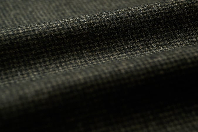 Close-up of dark grey-green wool flannel fabric with a fine micro-check texture, draped in soft folds