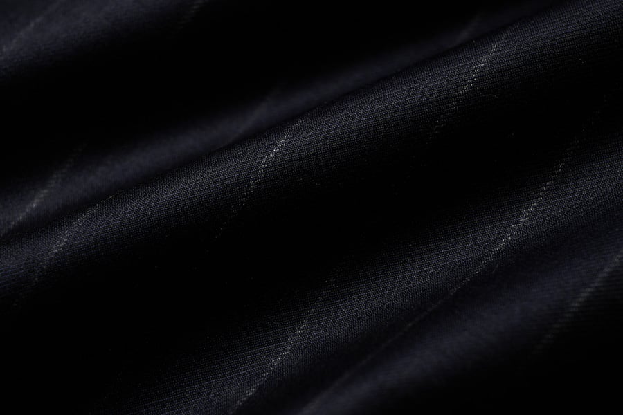Close-up of dark navy wool fabric with soft folds and thin, subtle pinstripes