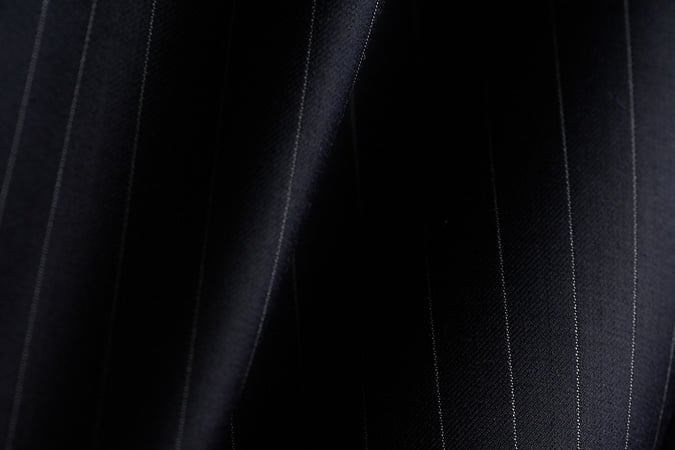 Close-up of dark navy wool fabric with thin white pinstripes, falling in soft folds