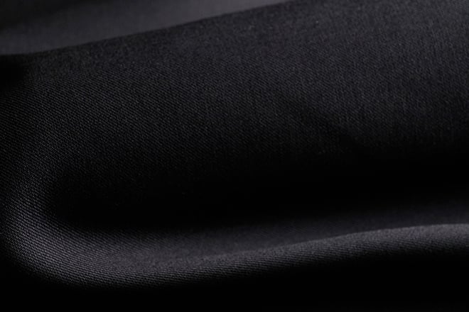 Close-up of black wool fabric with a fine twill weave, draped in soft folds under dramatic lighting