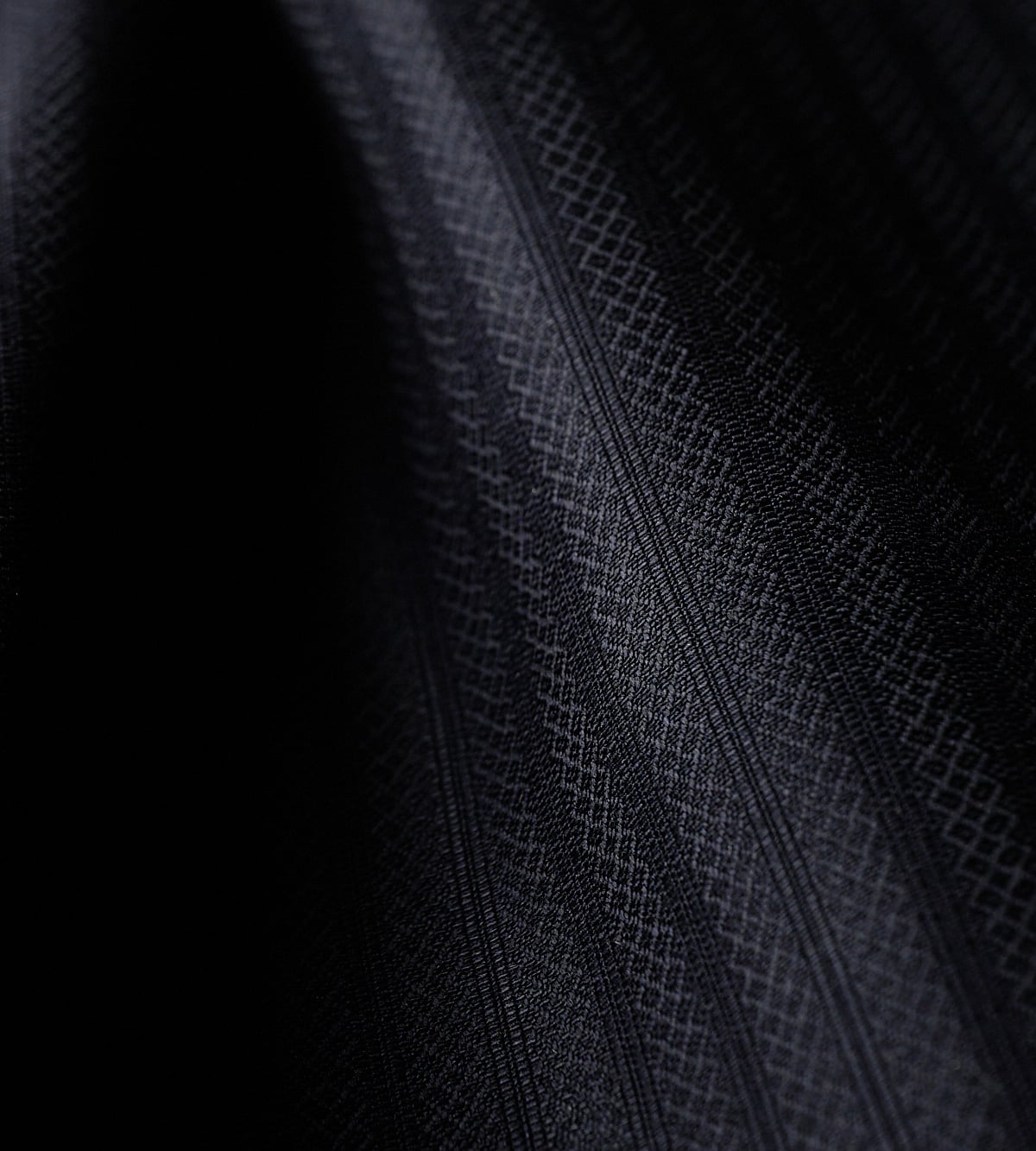 Close-up of dark charcoal wool fabric with a subtle diamond pattern and diagonal stripes in soft folds