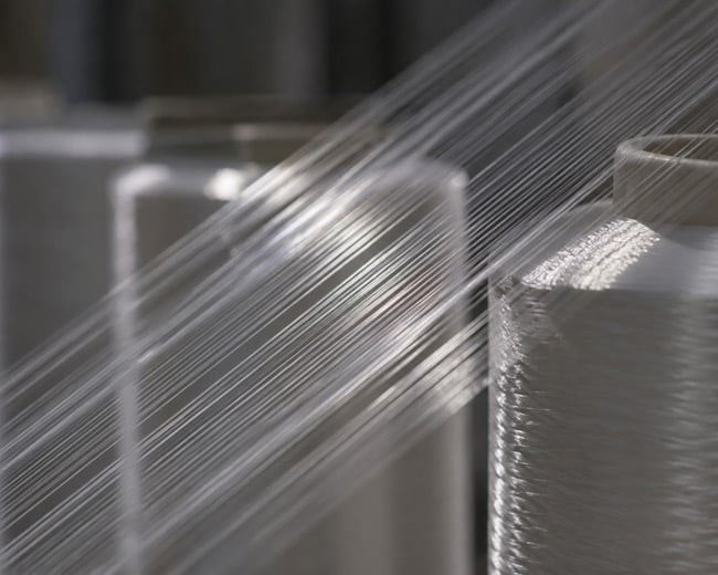 Fine white filaments stretching diagonally from large cylindrical yarn bobbins in a textile mill