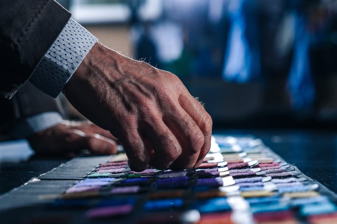Close-up of a man's hand in a suit sleeve touching a row of colorful fabric swatches on a dark table