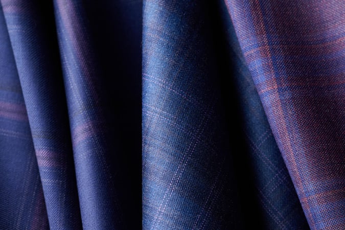 Draped blue wool fabric with a subtle purple and red check pattern, shown in close-up with soft folds